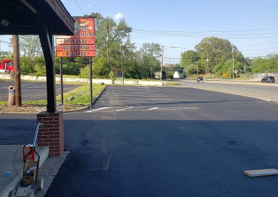 Small tavern parking lot with a sign reading "Open Daily, Food & Drink, Billiards," next to a road—expertly maintained by J&S Paving, providing quality paving services in Edgewood MD.