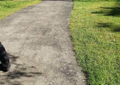 A gravel walking path bordered by green grass on a sunny day, with part of a person’s shoe visible—crafted with quality and care by J&S Paving, your experts in paving services.
