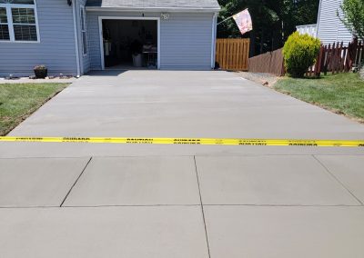 Freshly poured concrete driveway blocked off with caution tape in front of a suburban house and open garage, expertly completed by J&S Paving—your trusted paving services provider in Edgewood MD.