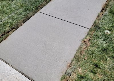Freshly poured concrete sidewalk surrounded by green grass on both sides under sunlight, expertly crafted by J&S Paving—your trusted choice for paving and asphalt services in Edgewood MD.