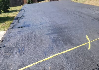 A freshly paved asphalt driveway by J&S Paving in Maryland is blocked by yellow caution tape, with grass lining both sides.