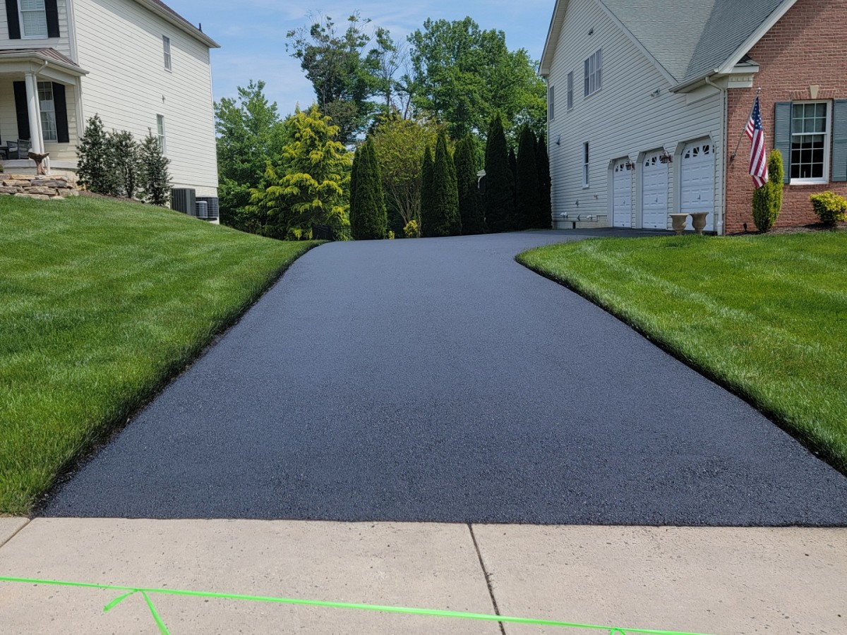 clp_64c076c4beecd A freshly paved black asphalt driveway by J&S Paving in Edgewood, MD stretches between two houses, bordered by neatly trimmed green grass.