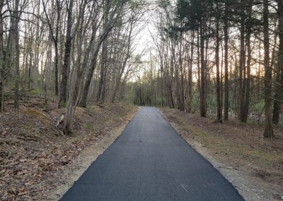 Paved path through a forested area with bare trees and soft sunlight in the background, showcasing quality paving services by J&S Paving.