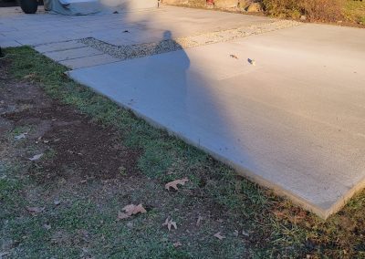 A shadow of a person stretches across a concrete slab in a sunlit backyard with some fallen leaves, highlighting the clean work typical of J&S Paving’s Asphalt Services in Edgewood MD.