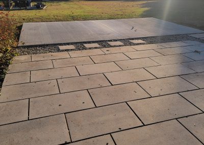 Concrete patio with paver stones by J&S Paving, a gravel strip, and a lawn area in the background on a sunny day—showcasing our expert paving services.
