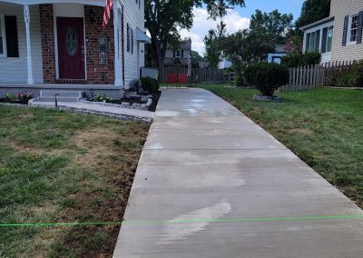Freshly poured concrete sidewalk leading to a house entrance in Maryland, with wet marks and green guide string visible—a testament to quality paving services.