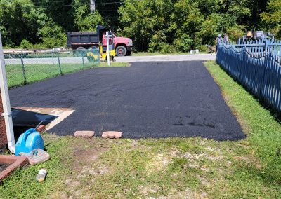 Freshly paved asphalt driveway with construction equipment and a red dump truck in the background, showcasing professional Asphalt Services in Maryland.