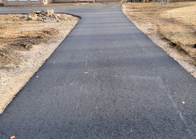 Freshly paved asphalt driveway leading up to a house, with dirt and grass on either side—a perfect example of quality Asphalt Services by J&S Paving.